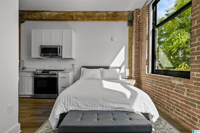 bedroom featuring brick wall, dark wood-style flooring, and beam ceiling