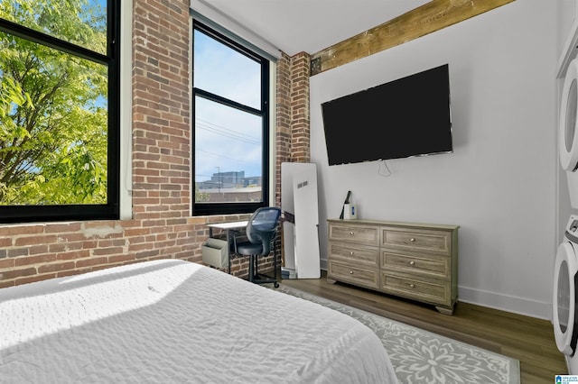 bedroom featuring brick wall, dark wood-style flooring, stacked washer / drying machine, and baseboards