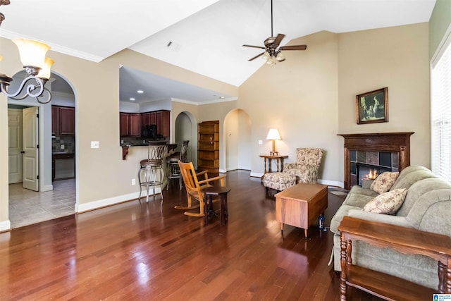 living area featuring baseboards, arched walkways, wood finished floors, ceiling fan with notable chandelier, and a tile fireplace