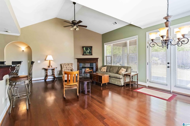 living room featuring a tiled fireplace, dark wood-style floors, vaulted ceiling, and ceiling fan with notable chandelier
