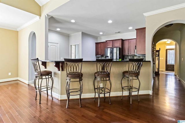 kitchen with stainless steel refrigerator with ice dispenser, ornamental molding, dark countertops, dark wood finished floors, and reddish brown cabinets