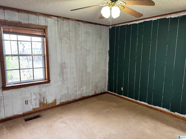 carpeted empty room with visible vents, a ceiling fan, and a textured ceiling