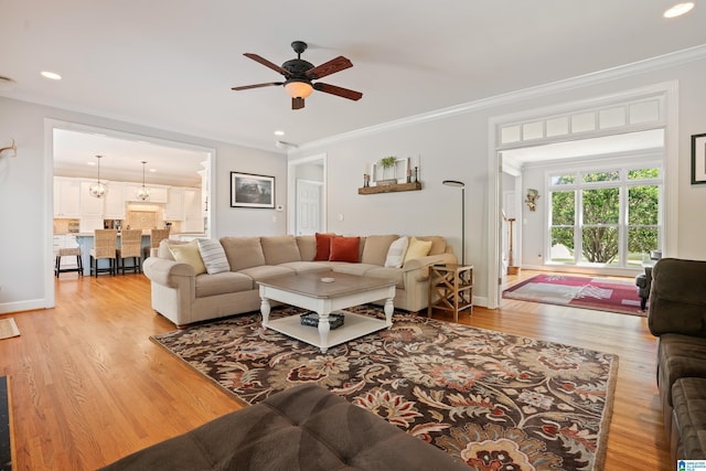 living area featuring light wood-type flooring, a ceiling fan, baseboards, and crown molding