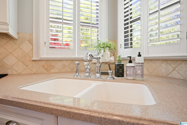 room details with backsplash, white cabinets, and a sink