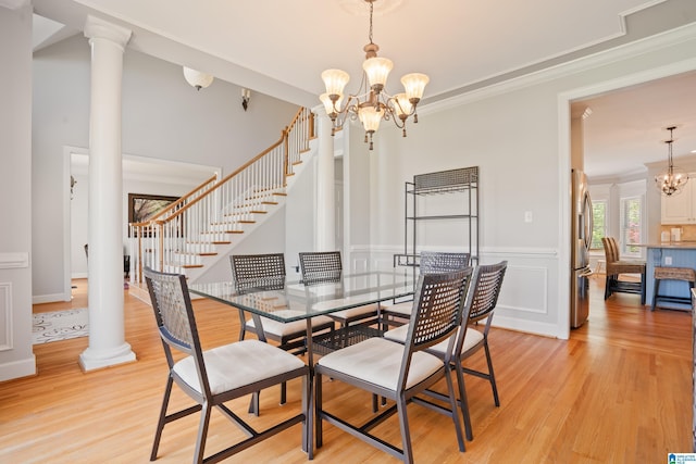 dining area with a chandelier, stairway, light wood finished floors, and ornate columns