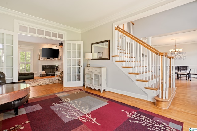 living area featuring crown molding, stairs, wood finished floors, ceiling fan with notable chandelier, and a fireplace