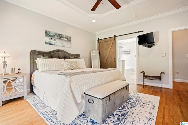 bedroom featuring crown molding, light wood-style flooring, connected bathroom, and a barn door