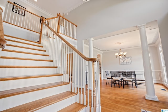 staircase featuring crown molding, wood finished floors, an inviting chandelier, visible vents, and ornate columns