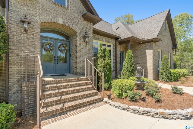 doorway to property featuring french doors, brick siding, and roof with shingles