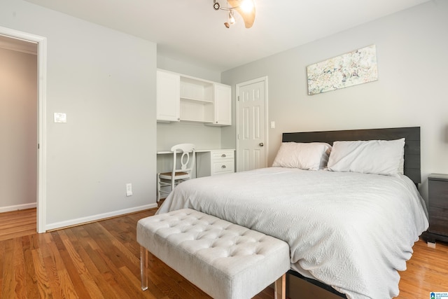 bedroom with built in study area, baseboards, and light wood-style flooring