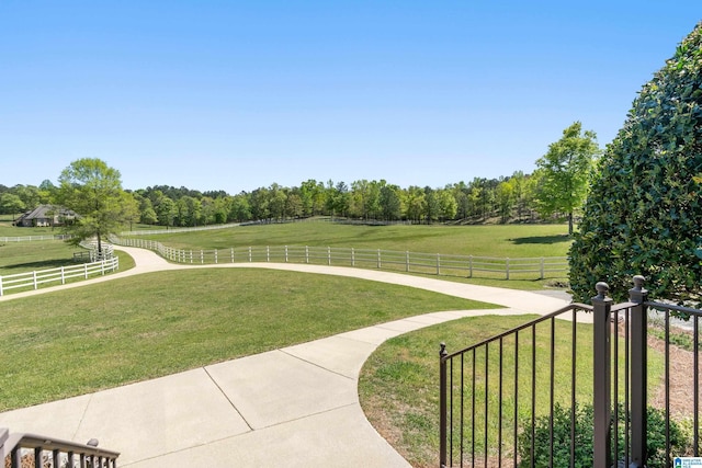 view of property's community with a rural view, a yard, and fence