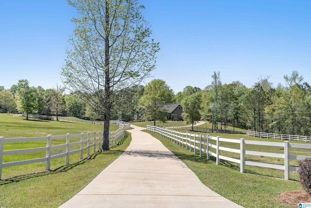 view of community with fence, a lawn, a rural view, and driveway