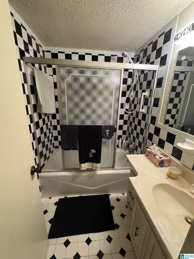 bathroom with combined bath / shower with glass door, vanity, tile patterned floors, a textured ceiling, and tile walls