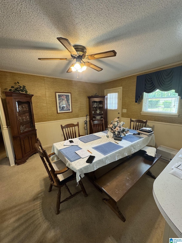 dining area with ceiling fan, light carpet, a wainscoted wall, and a textured ceiling