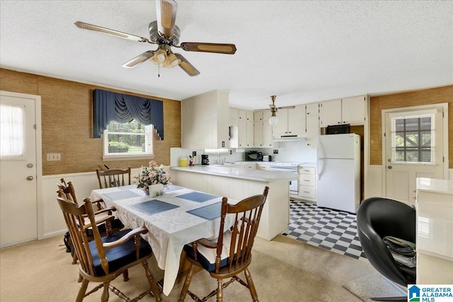 dining space with a textured ceiling, a healthy amount of sunlight, a wainscoted wall, and wallpapered walls