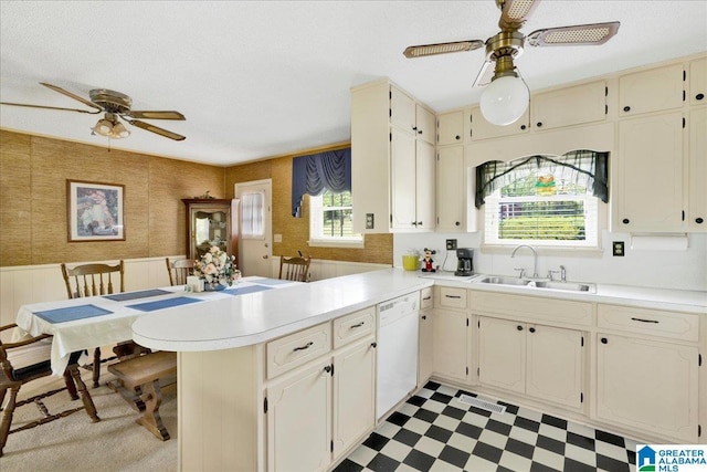 kitchen featuring a ceiling fan, a sink, dishwasher, light floors, and a peninsula
