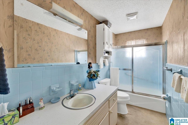 bathroom featuring wallpapered walls, vanity, tile walls, toilet, and shower / bath combination with glass door