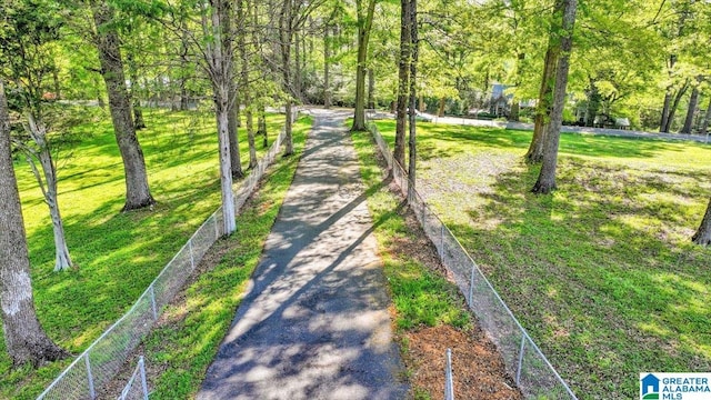 view of property's community with aphalt driveway, fence, and a yard