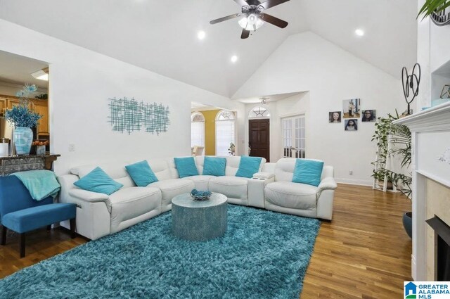 living area with ceiling fan, wood finished floors, a fireplace, and high vaulted ceiling