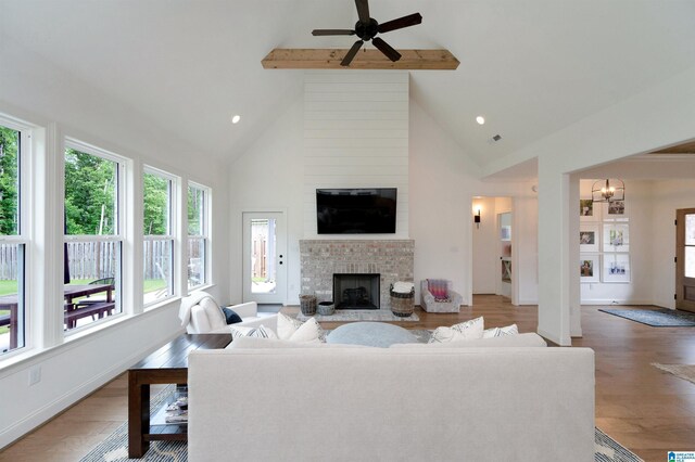 living area featuring beam ceiling, a fireplace, ceiling fan, high vaulted ceiling, and light wood-style flooring