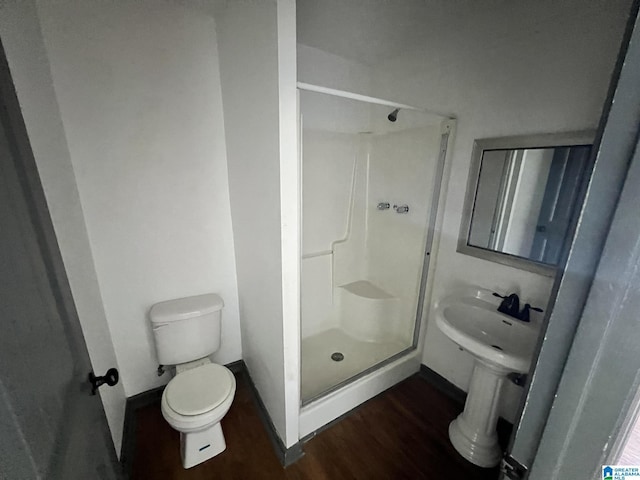 bathroom with a shower stall, wood finished floors, baseboards, and toilet