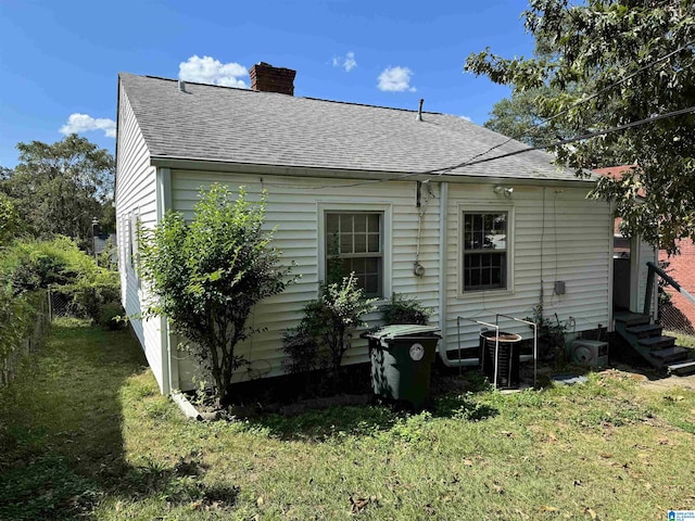 rear view of house with a shingled roof, a yard, entry steps, a chimney, and fence