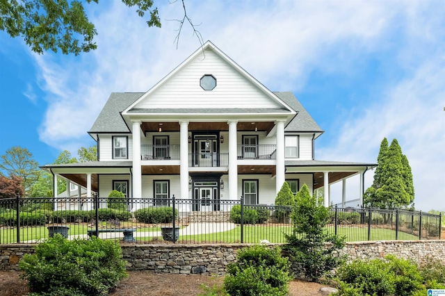 neoclassical home featuring a porch, roof with shingles, a balcony, and a fenced front yard