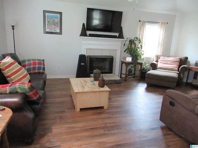 living area featuring baseboards, a ceiling fan, a fireplace, and dark wood finished floors