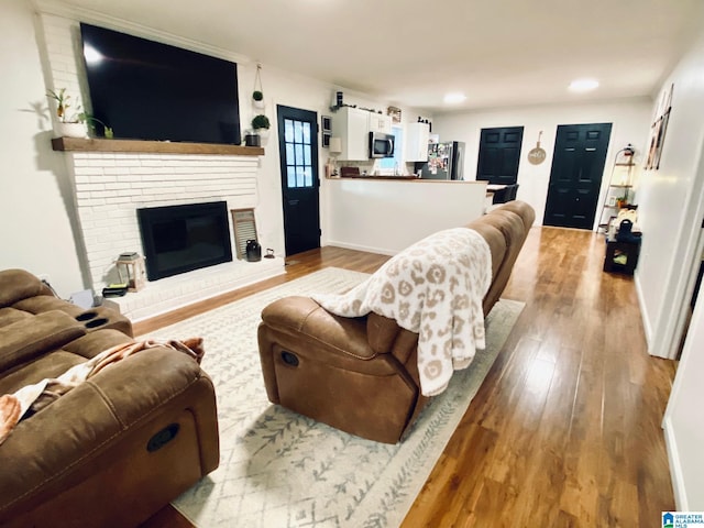 living room featuring recessed lighting, a brick fireplace, and wood finished floors