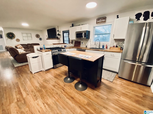 kitchen with a sink, open floor plan, light wood-style floors, butcher block counters, and stainless steel appliances