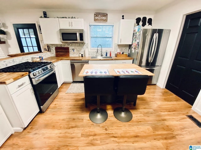 kitchen featuring stainless steel appliances, butcher block countertops, light wood-style floors, and a sink