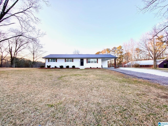 ranch-style house featuring aphalt driveway, an attached carport, a front lawn, and metal roof