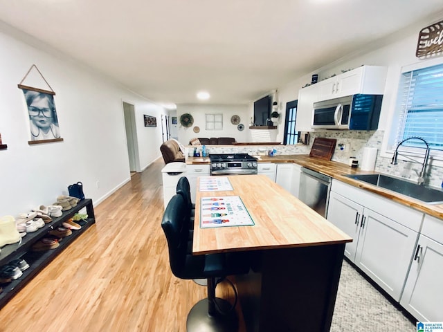 kitchen with light wood-type flooring, a peninsula, butcher block counters, stainless steel appliances, and a sink