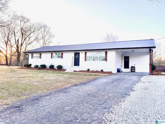 ranch-style home featuring an attached carport, a front yard, metal roof, and driveway