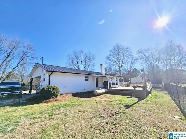 rear view of house featuring a standing seam roof, a lawn, metal roof, fence, and a chimney