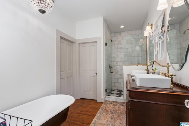 bathroom with wood finished floors, a sink, a stall shower, a freestanding tub, and recessed lighting