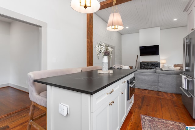 kitchen with dark wood-style floors, a breakfast bar, dark countertops, appliances with stainless steel finishes, and white cabinetry