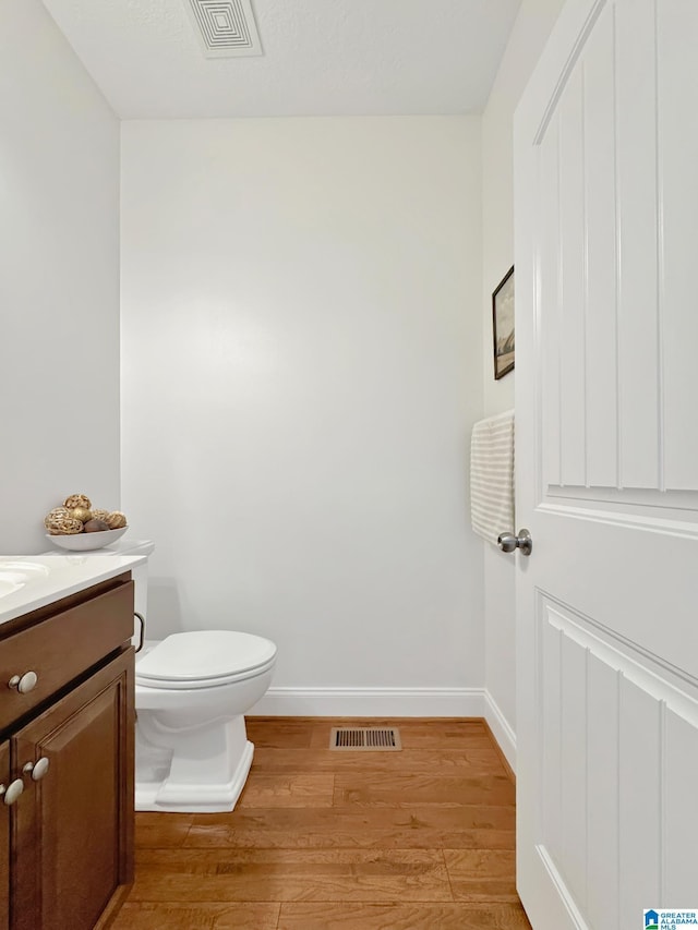 bathroom with toilet, wood finished floors, visible vents, and baseboards