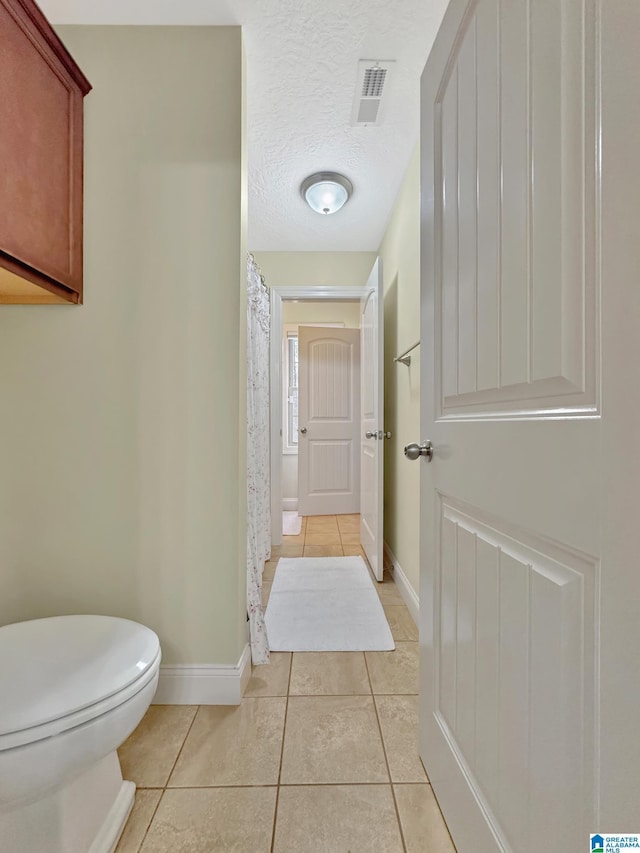bathroom featuring tile patterned floors, visible vents, toilet, baseboards, and a shower with shower curtain