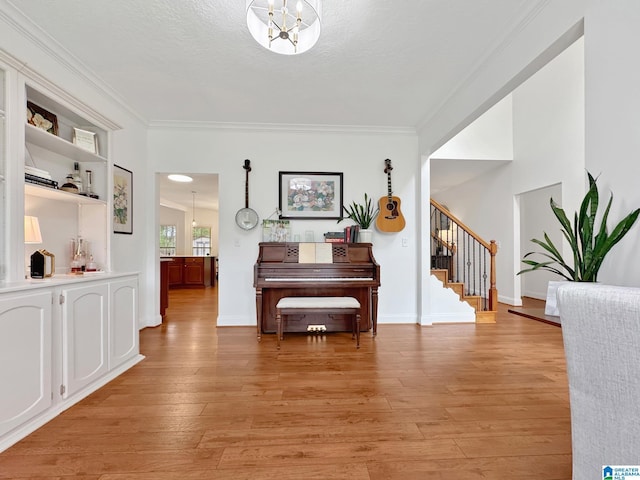 hallway with light wood finished floors, crown molding, baseboards, a chandelier, and stairs