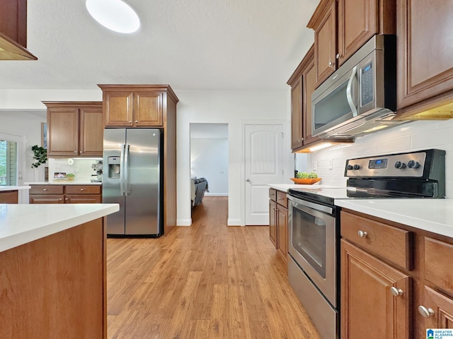 kitchen with brown cabinetry, decorative backsplash, light wood-type flooring, stainless steel appliances, and light countertops