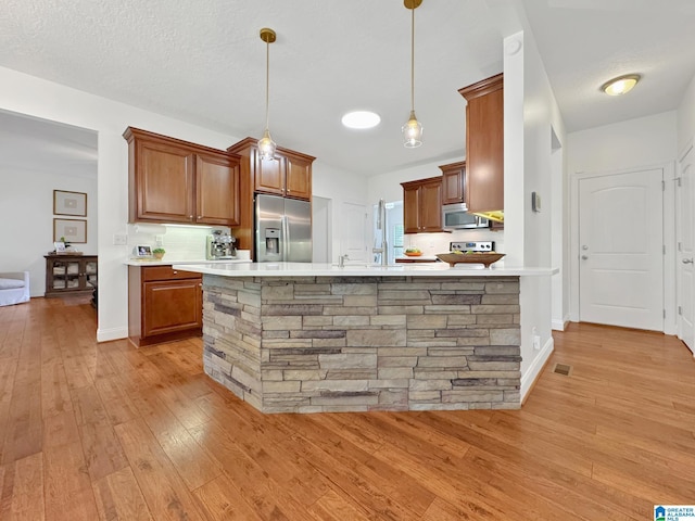 kitchen with brown cabinetry, stainless steel appliances, light wood finished floors, light countertops, and decorative light fixtures