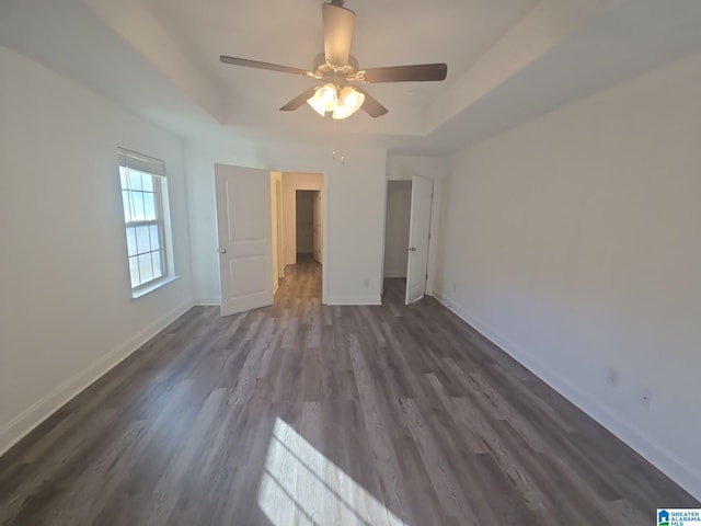 unfurnished bedroom with dark wood-type flooring, a tray ceiling, baseboards, and ceiling fan