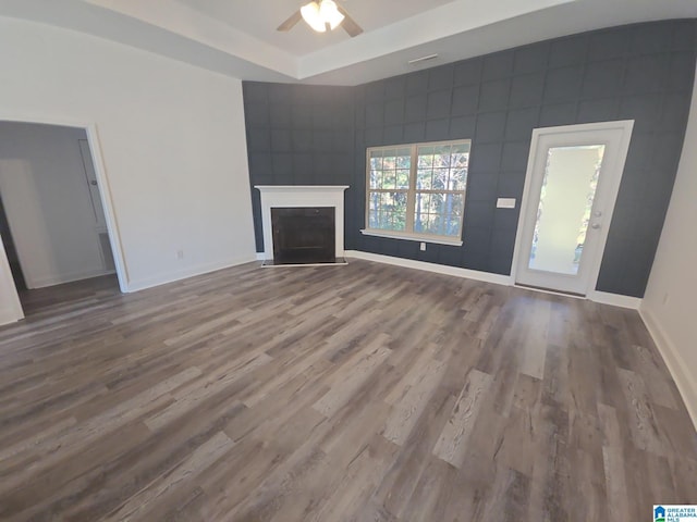 unfurnished living room with baseboards, a fireplace, a tray ceiling, ceiling fan, and wood finished floors