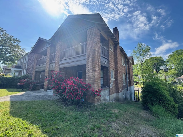 view of side of property featuring a chimney, brick siding, a yard, and a balcony