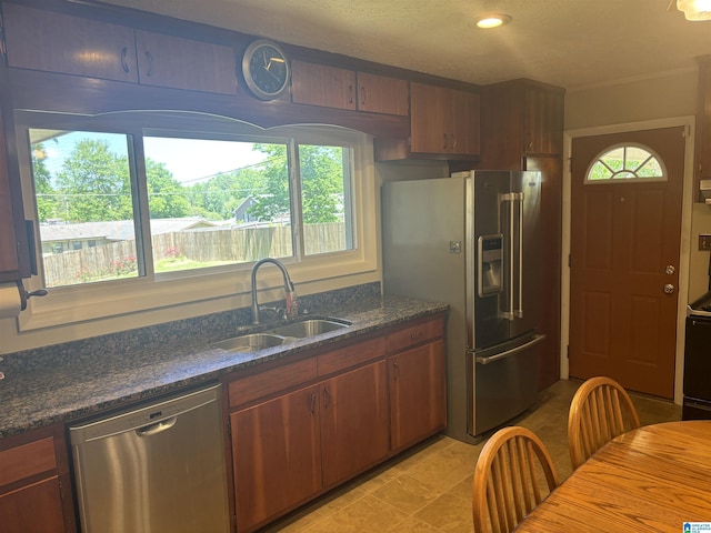 kitchen with dark stone counters, a sink, light tile patterned floors, brown cabinetry, and appliances with stainless steel finishes