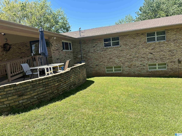 back of house with a lawn, roof with shingles, and brick siding