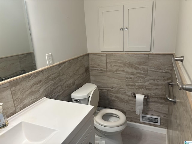 half bath with tile walls, visible vents, a wainscoted wall, and toilet