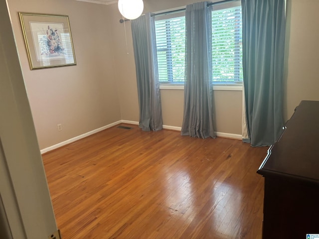 spare room featuring wood finished floors, visible vents, and baseboards