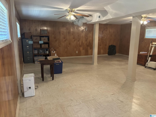 basement featuring baseboards, wood walls, visible vents, and a ceiling fan